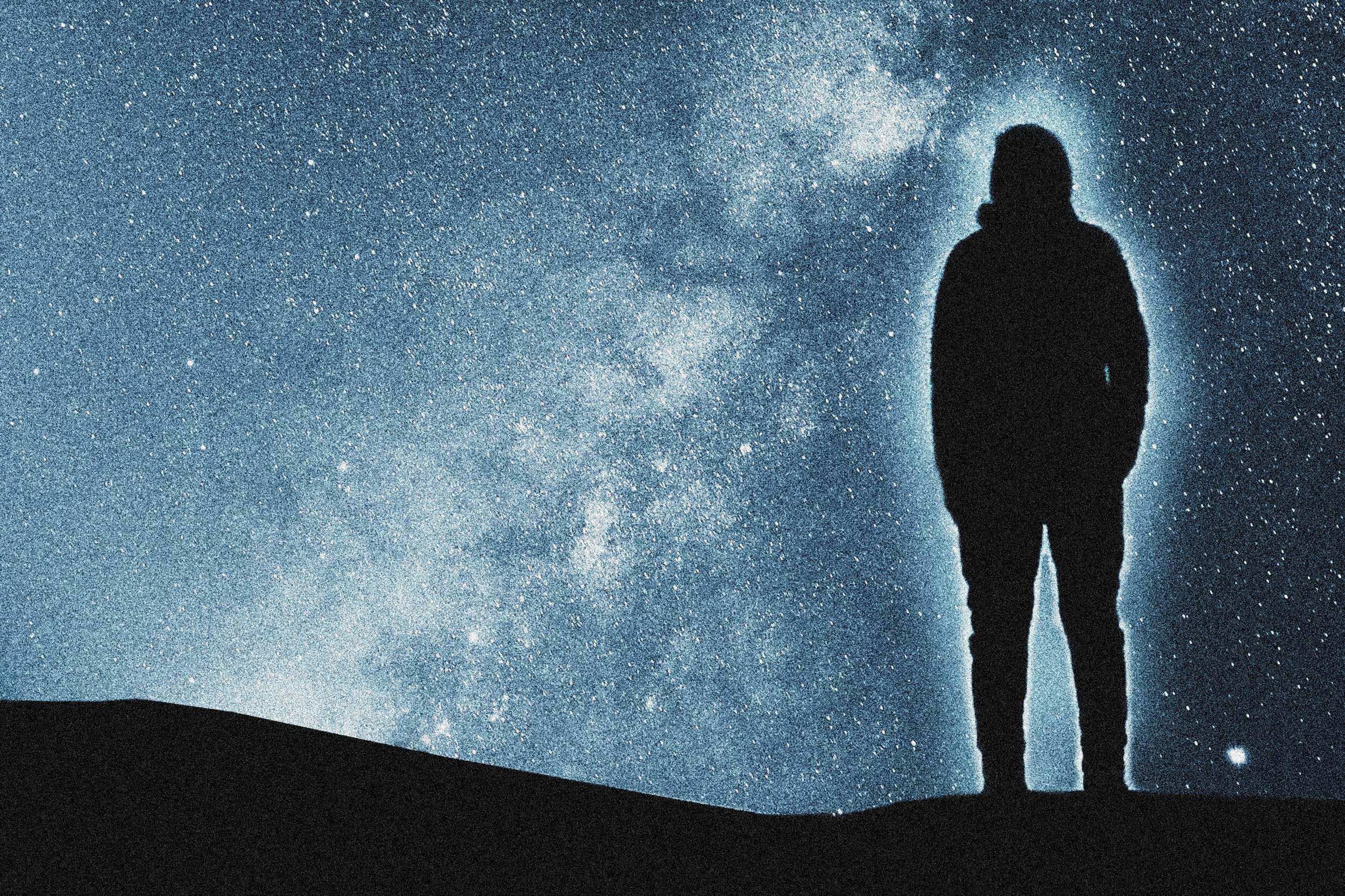 Ein von einer Aura umgebener Mensch schaut nachdenklich in den Sternenhimmel, der einen Teil der Galaxie zeigt.